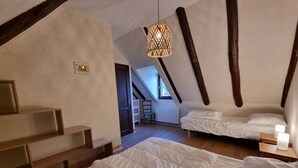Une chambre avec un grand lit, un plus petit lit et une chaise. Un escalier mène à un niveau supérieur.
