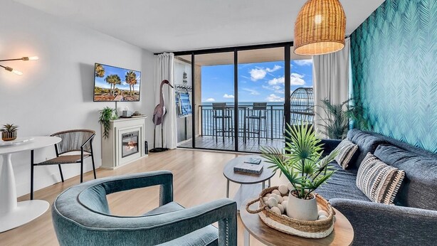 Ein modernes Wohnzimmer mit Sofa, Sesseln, Kamin und einem Balkon mit Meerblick.