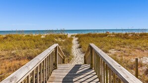 Ein hölzerner Steg führt zu einem Strand bei blauem Himmel.