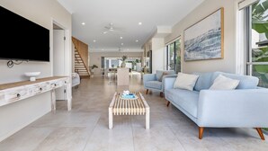 A spacious living area with a flat-screen TV, a light blue sofa, a coffee table, and a staircase leading to an outdoor patio. - Casa Casuarina - Private pool & steps to the beach (Casuarina)