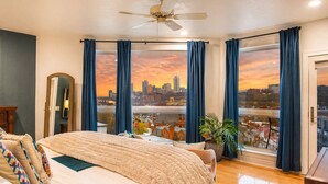 A bedroom with a city view, a bed, a ceiling fan, and a large window with curtains. - ★HostWise Stays★ Rooftop Deck | Garage | Balcony Views | Upscale! (Pittsburgh)