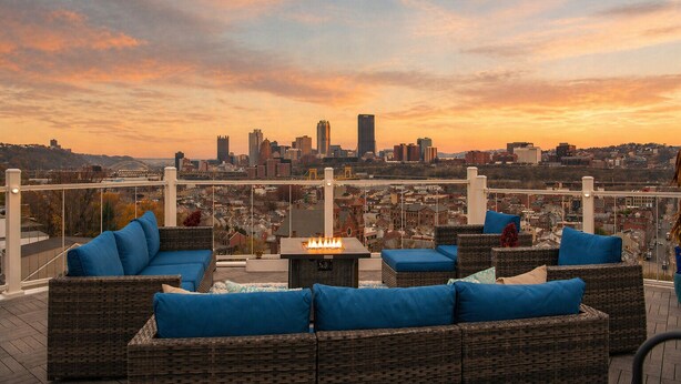 A rooftop terrace with wicker furniture, a fire feature, and a city skyline view. - ★HostWise Stays★ Rooftop Deck | Garage | Balcony Views | Upscale! (Pittsburgh)