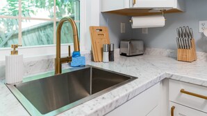 A modern kitchen with a stainless steel sink, white cabinets, a wooden cutting board, and a knife block. - Sunset Suites (Old Orchard Beach)