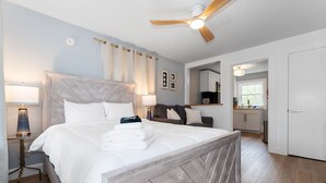 A bedroom with a large bed, a wooden headboard, a ceiling fan, and a nightstand with a lamp. - Sunset Suites (Old Orchard Beach)
