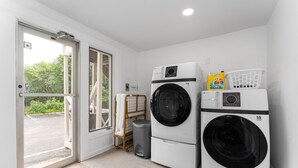 A laundry room with two front-loading washing machines, a trash bin, and a laundry basket on the wall. - Sunset Suites (Old Orchard Beach)