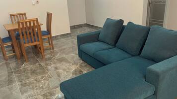 A living room with a blue sofa, wooden chairs, and a tiled floor.