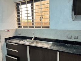 A kitchen with a stainless steel sink, a window with metal bars, and a black countertop.