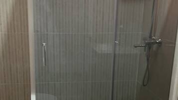 A glass-enclosed shower stall with a handheld showerhead, a white toilet, and a tiled floor.