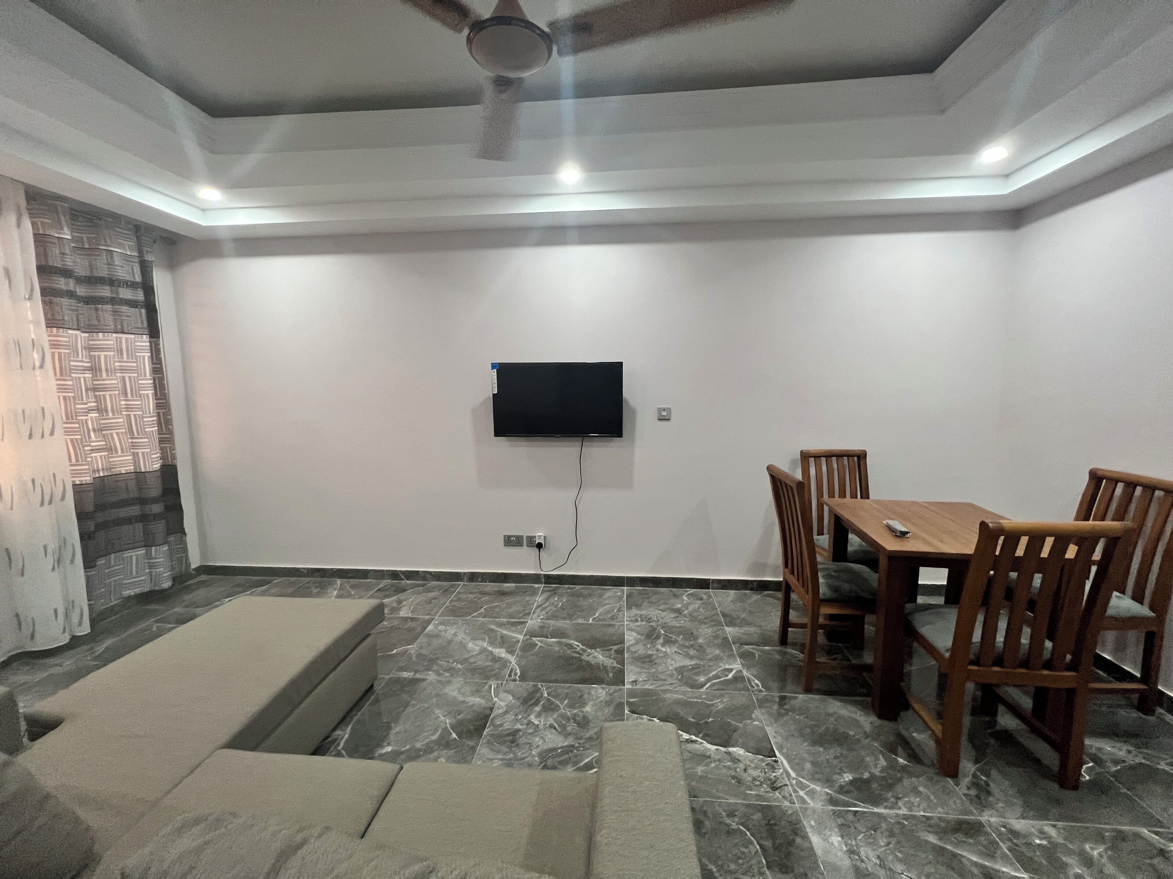 Una sala de estar con un televisor montado en la pared, una mesa de comedor con sillas y un sofá.