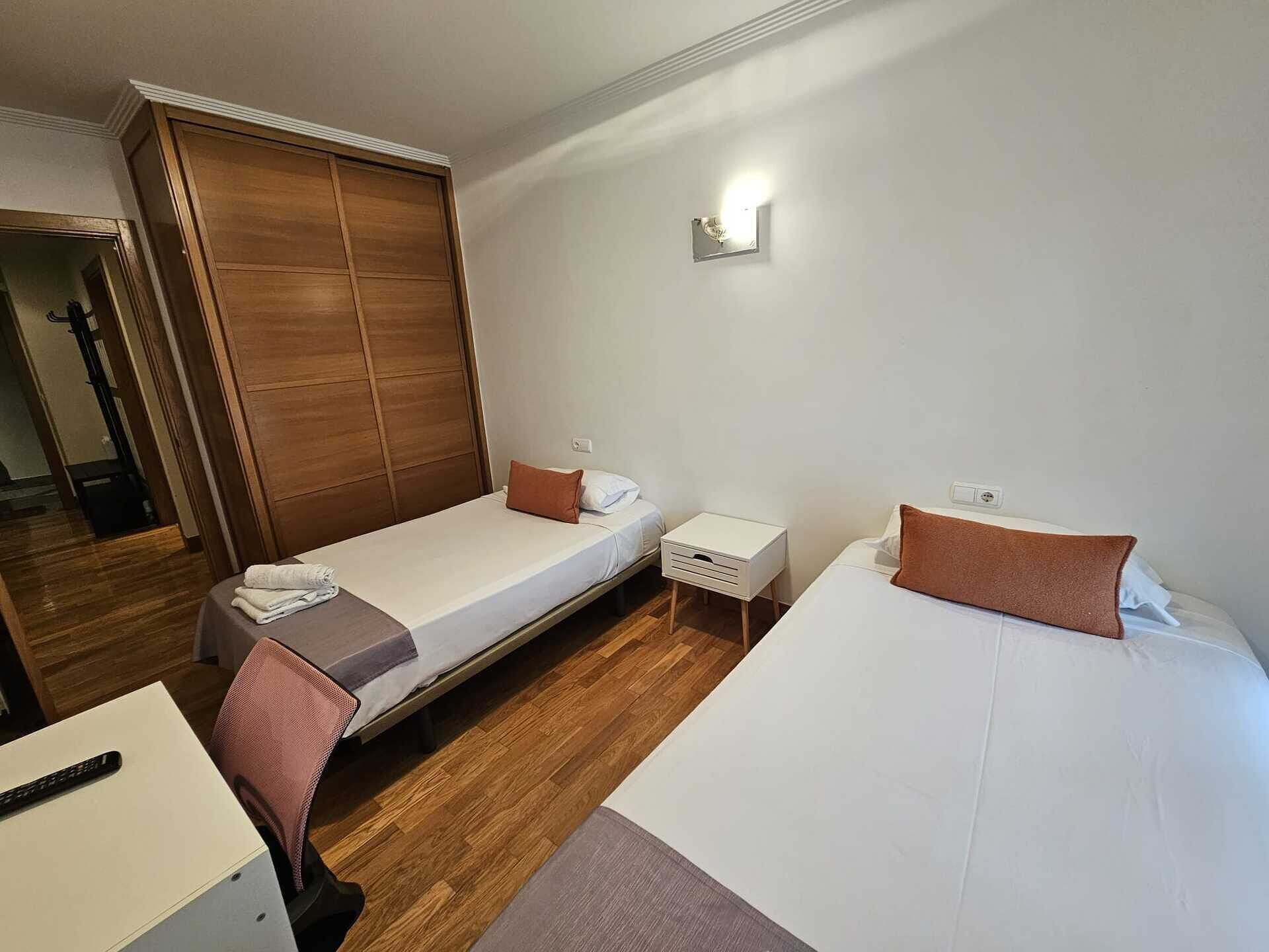 Ein Hotelzimmer mit zwei Einzelbetten, einem Holzschrank, einem kleinen Nachttisch und einem Schreibtisch mit Stuhl.