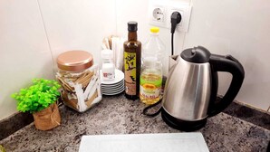 Una encimera de cocina con una tabla de cortar, una tetera, una botella de aceite, un tarro de té, una planta pequeña y algunos platos.