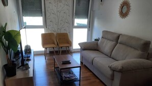 Un salón con un sofá, dos sillones, una mesita de centro, un televisor, una planta y un extintor.