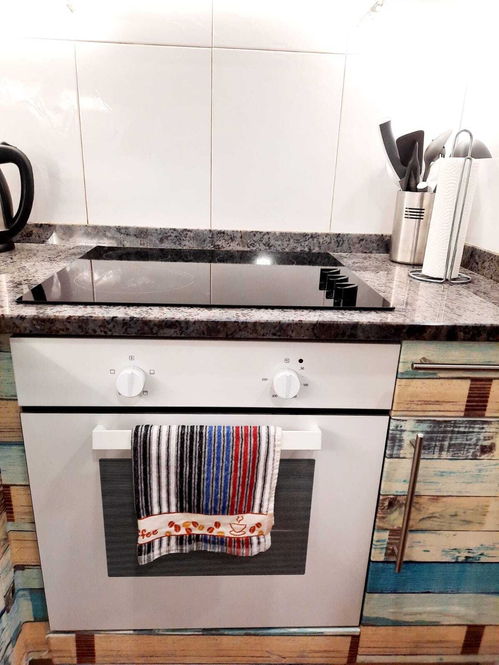 A kitchen with a black stovetop, white cabinets, and a towel hanging on the oven door.