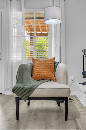 A chair with a cushion, a blanket, and a lamp in a room with a window and a door.