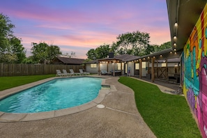 A backyard with a swimming pool, a covered patio area, and a wooden fence.