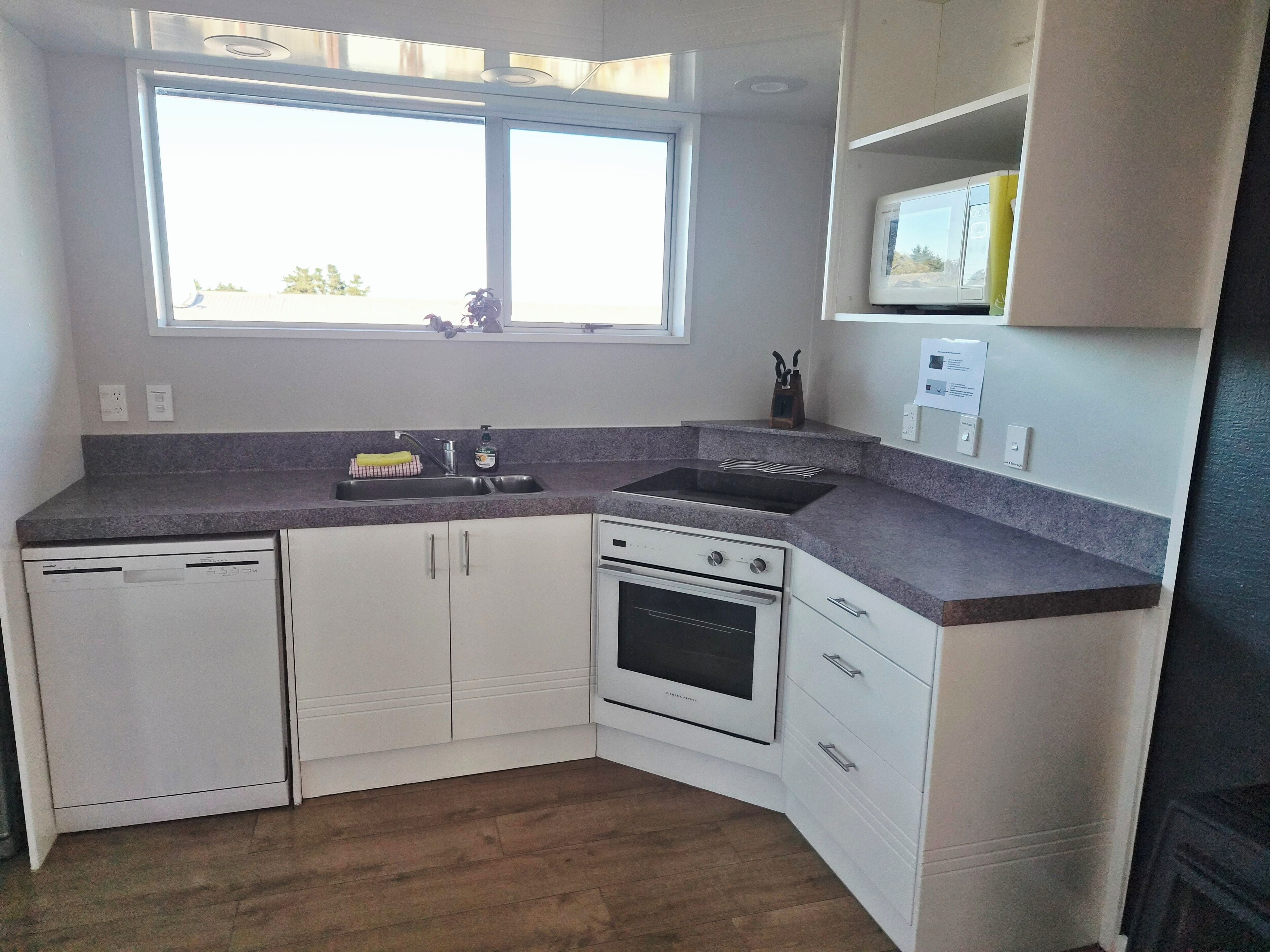 A kitchen with white cabinets, a built-in oven, a sink, and a window above the sink.