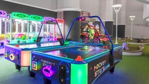 En lystig indendørs spillehal med flere kranautomater og et bord med et hockeytema.