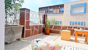 A rooftop terrace with a stone wall, potted plants, a wicker ottoman, and a small table. - Superior Double with Terrace #1 (Tamraght Ouzdar,)