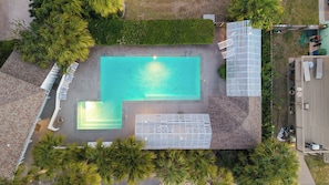 Vue aérienne d’un espace piscine avec une terrasse en bois, un patio clôturé et une végétation luxuriante tout autour.
