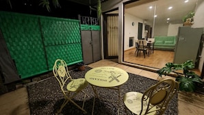 Een eetgedeelte met een tafel en stoelen, een groene wand en een glazen schuifdeur naar een woonkamer.