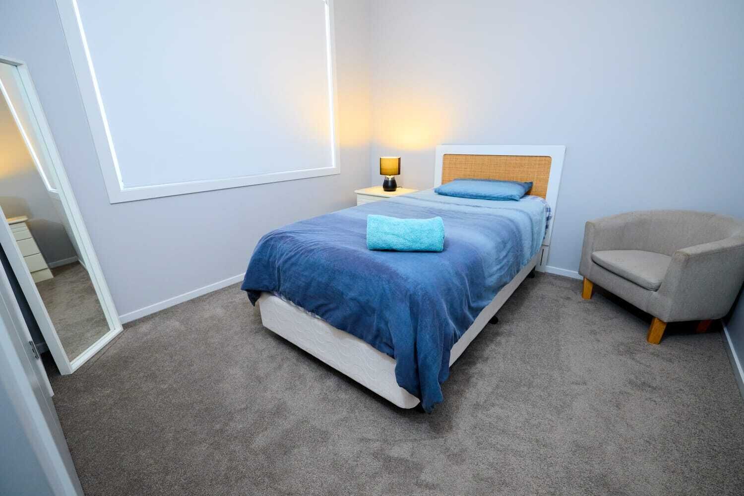 Een slaapkamer met een bed, bedlampje, stoel en een spiegel.