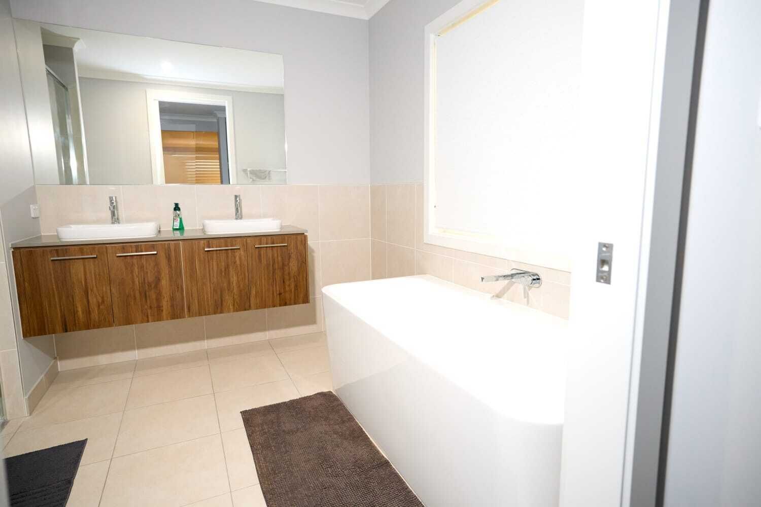 Ein Badezimmer mit einer weißen Badewanne, zwei Waschbecken, Holzschränken, einem Spiegel und einem Fenster.