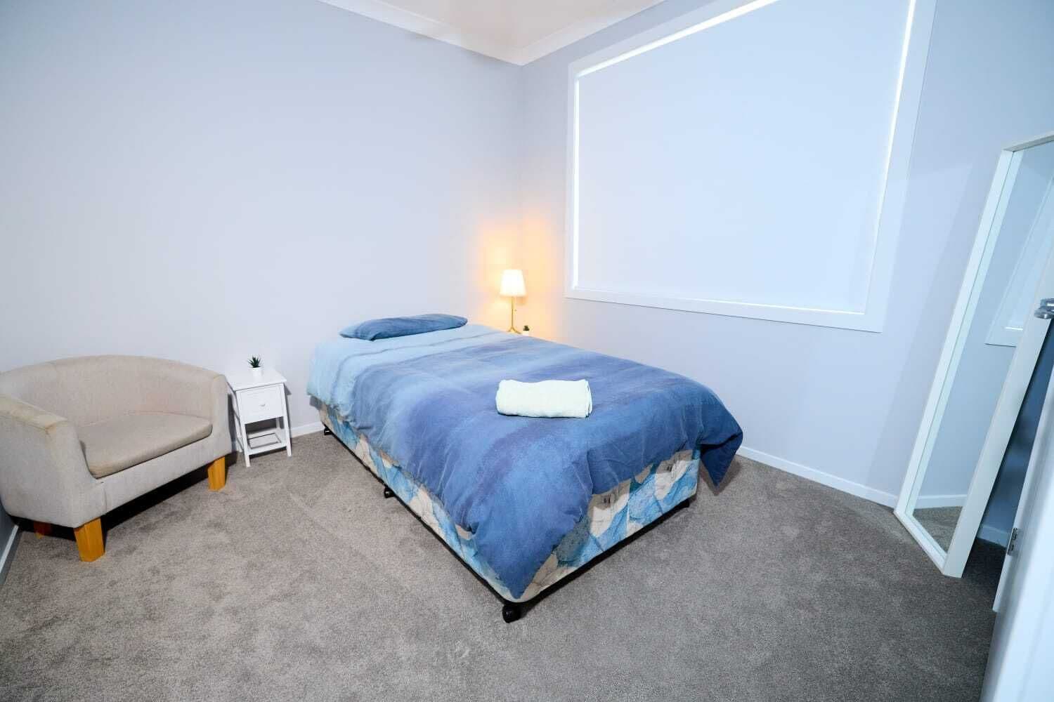A bedroom with a bed, a chair, a nightstand, a lamp, and a door.