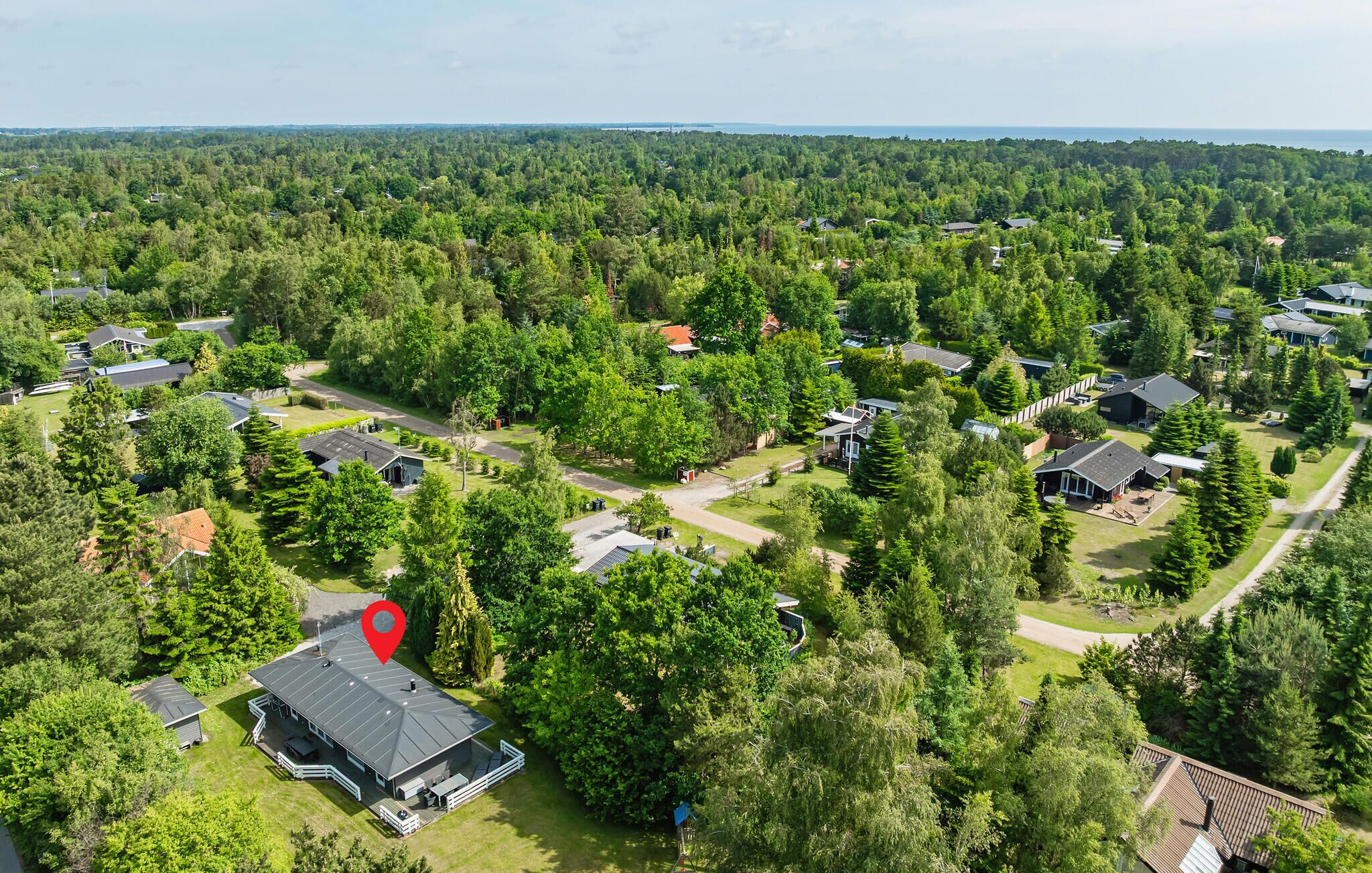 An aerial view of a residential area with houses surrounded by dense greenery and a body of water in the distance.