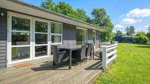 Een overdekt terras buiten, met een tafel en stoelen, een houten terras en een gazon.