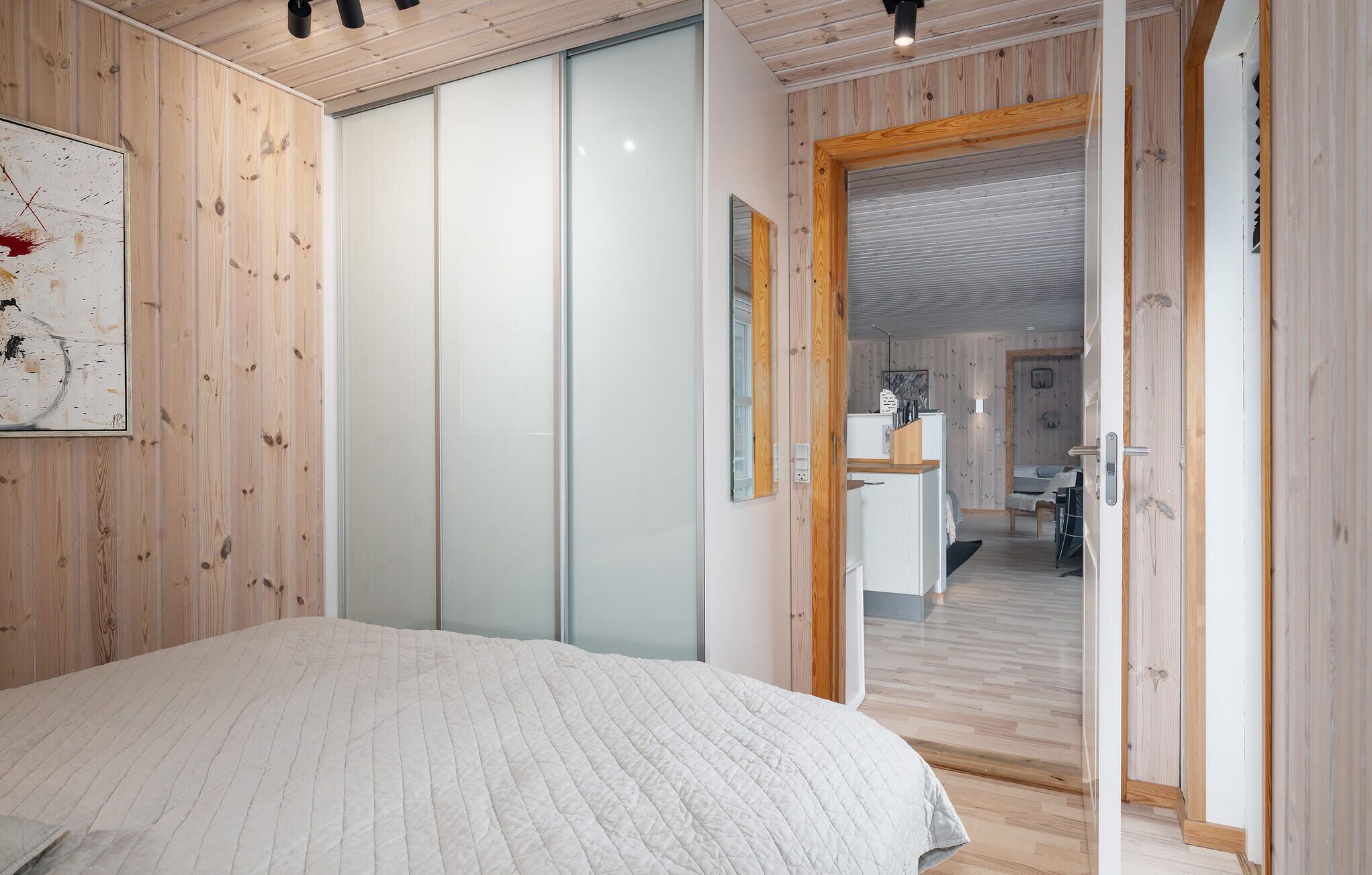 A bedroom with a large bed, wooden walls, a sliding door, and a view into the living area.