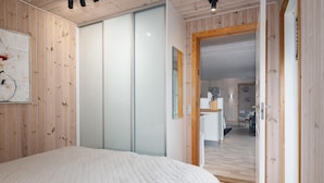 Een slaapkamer met een groot bed, houten wanden, een schuifdeur en uitzicht op de woonkamer.