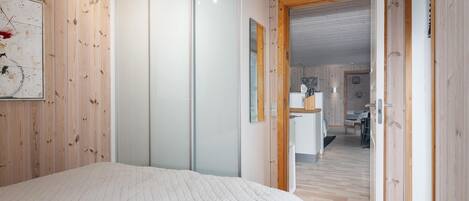 A bedroom with a large bed, wooden walls, a sliding door, and a view into the living area.