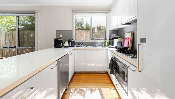 Una cocina moderna con armarios blancos, encimera de madera, horno empotrado y ventana que aporta luz natural.