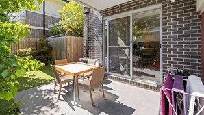 Un patio con una mesa y sillas, una puerta corrediza de vidrio y una valla de madera.