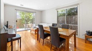 Un comedor espacioso con una mesa y sillas de madera, una laptop sobre un escritorio, y un ventanal con vistas al exterior.