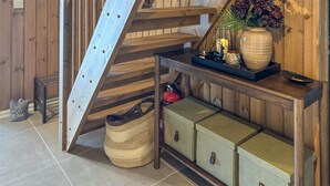 Een houten trap met een metalen leuning, een rieten mand, een brandblusser en een console tafel met decoratieve objecten.