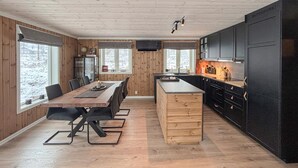 Een moderne keuken met een houten eettafel en stoelen, een vast aanrecht en zwarte kastjes.