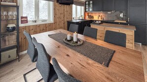 Een eetruimte met een houten tafel, gestoffeerde grijze stoelen en een kaarsdecoratie.