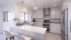 A modern kitchen with white cabinetry, stainless steel appliances, and a central island with seating. - Charming 3-bedroom condo with AC in San Clemente (San Clemente)