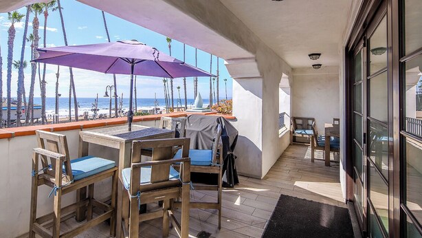A balcony with wooden chairs and a purple umbrella, overlooking a beach with palm trees and the ocean. - Charming 3-bedroom condo with AC in San Clemente (San Clemente)