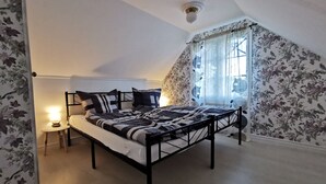 A bedroom with a bed, a nightstand, a lamp, and a window with floral curtains. - Vacation home in southern Sweden-Hus Gammal Dam (pet hair free) for up to 6 people (Eringsboda)