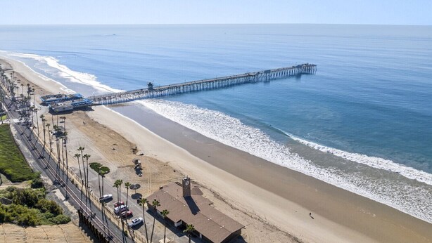 A beach with a long pier extending into the ocean, a sandy shoreline, and a road with parked cars and palm trees. - Hideaway 4Plex! Walk to the beach, Downtown, AC! (San Clemente)