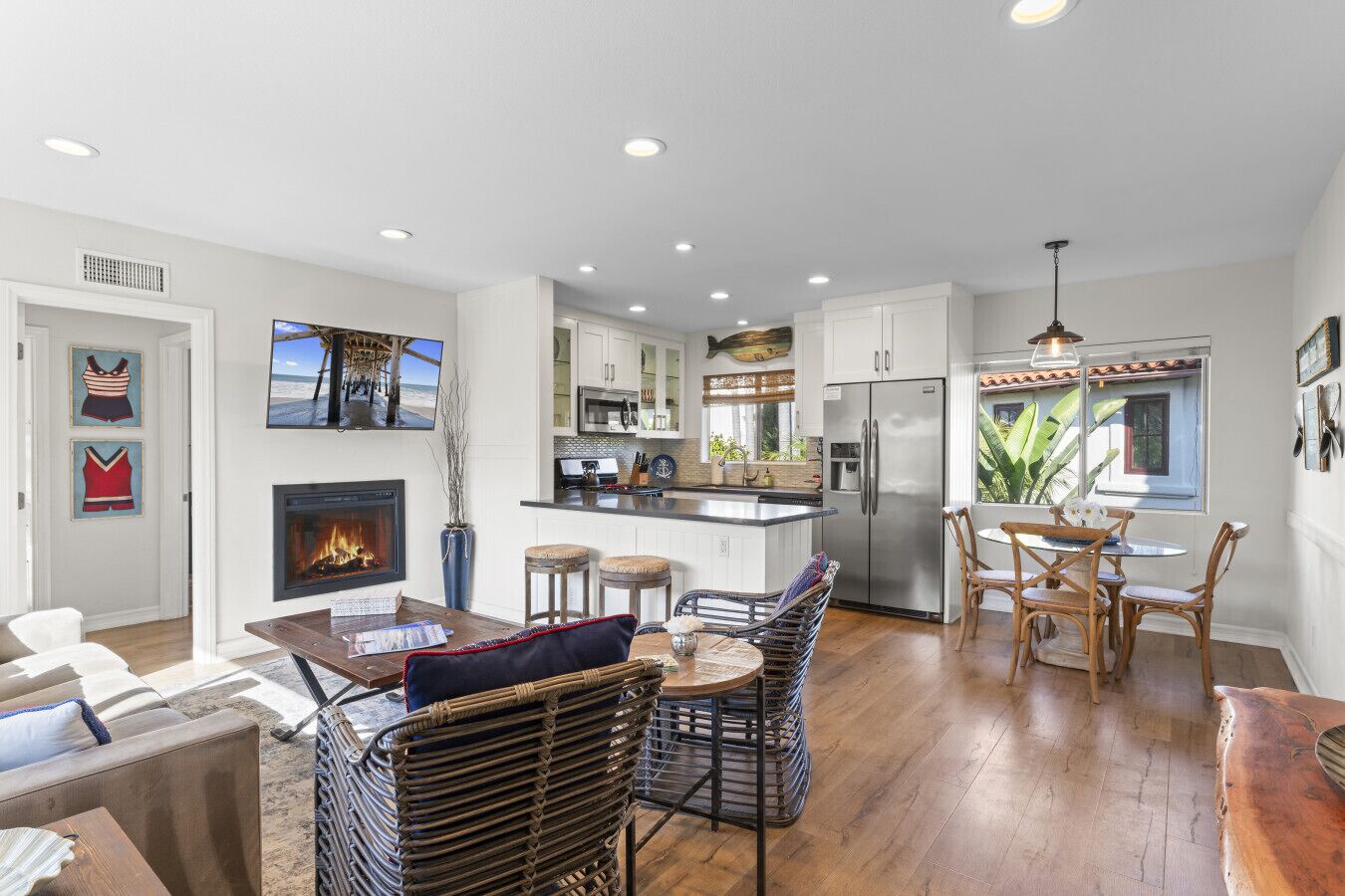 A modern kitchen with white cabinets, a stainless steel refrigerator, and a dining area with wicker chairs and a wooden table.
