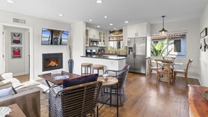 A modern kitchen with white cabinets, a stainless steel refrigerator, and a dining area with wicker chairs and a wooden table. - Hideaway 4Plex! Walk to the beach, Downtown, AC! (San Clemente)