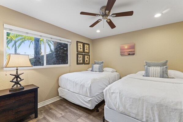 Bright bedroom w/ two beds, ceiling fan & window views bringing in natural light