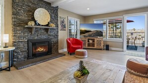 Un salon avec une cheminée en pierre, un fauteuil rouge, un téléviseur à écran plat et une vue sur l’extérieur.