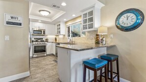 Una cocina moderna con armarios blancos, una isla central con taburetes, un microondas, un horno y un fregadero.