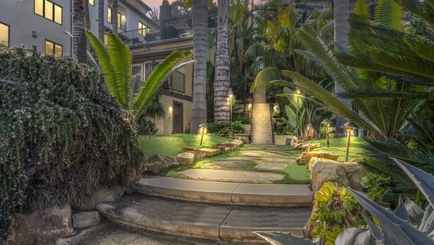 A well-maintained garden with a stone pathway leading to a staircase, surrounded by tropical plants and palm trees. - Coastal townhouse w/ AC, BBQ & shared beach access (San Clemente)