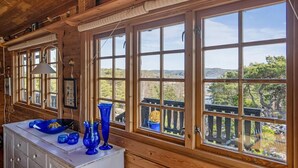 L’intérieur d’un chalet en bois, avec de grandes fenêtres, une commode blanche et de la verrerie bleue.