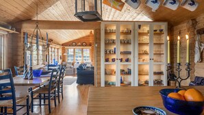 L’intérieur chaleureux d’un chalet comprend un coin repas, un salon et un grand buffet rempli de vaisselle et de verres.